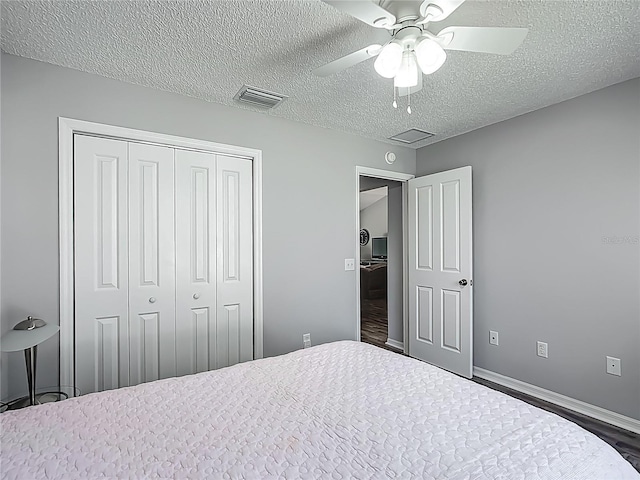 bedroom with a textured ceiling, baseboards, wood finished floors, visible vents, and a closet