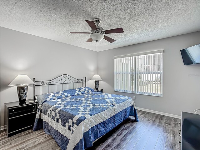 bedroom featuring baseboards, a textured ceiling, ceiling fan, and wood finished floors
