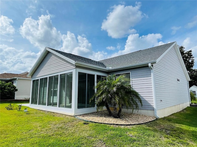 back of house featuring a sunroom, a shingled roof, and a lawn