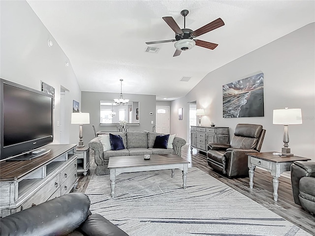 living area with ceiling fan with notable chandelier, vaulted ceiling, wood finished floors, and visible vents