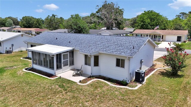 11118 SW 76th Ave, Ocala, FL 34476 - rear view of house featuring a shingled roof, a sunroom, a lawn, a patio, and central AC unit