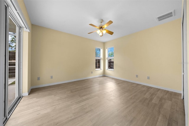 empty room with visible vents, a wealth of natural light, a ceiling fan, and light wood finished floors