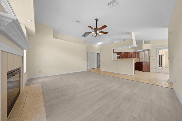 unfurnished living room with baseboards, light wood-type flooring, a fireplace, a ceiling fan, and visible vents