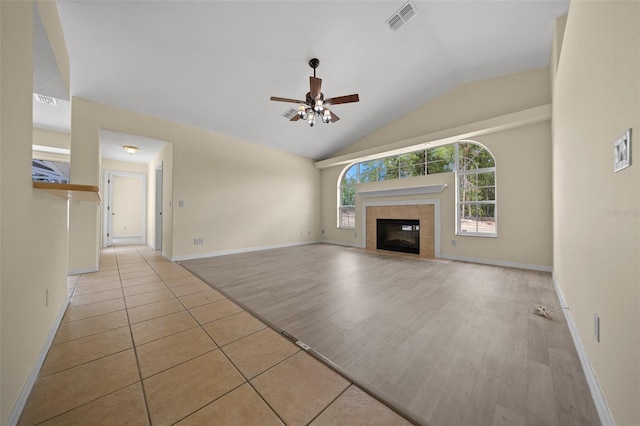 unfurnished living room featuring vaulted ceiling, light tile patterned floors, a ceiling fan, visible vents, and a tile fireplace