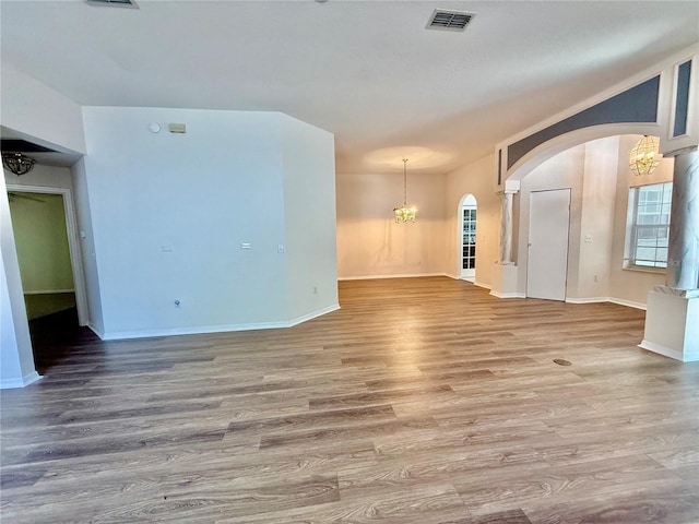 spare room with visible vents, baseboards, arched walkways, a notable chandelier, and wood finished floors