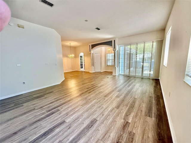 unfurnished living room with baseboards, an inviting chandelier, visible vents, arched walkways, and wood finished floors