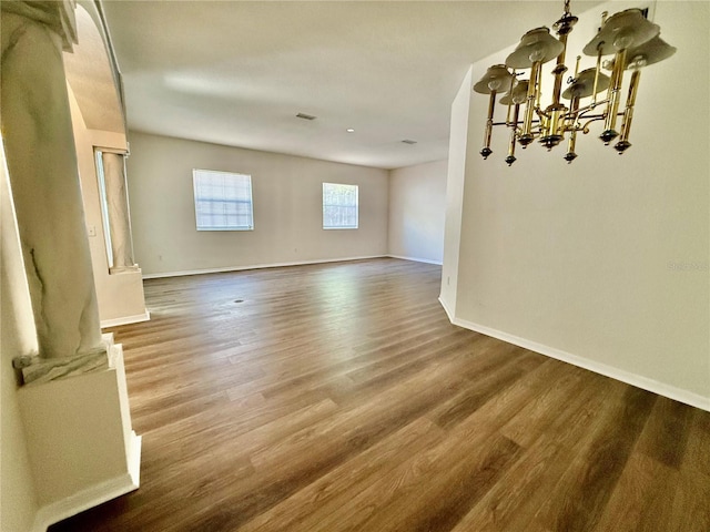 spare room featuring visible vents, baseboards, an inviting chandelier, and wood finished floors
