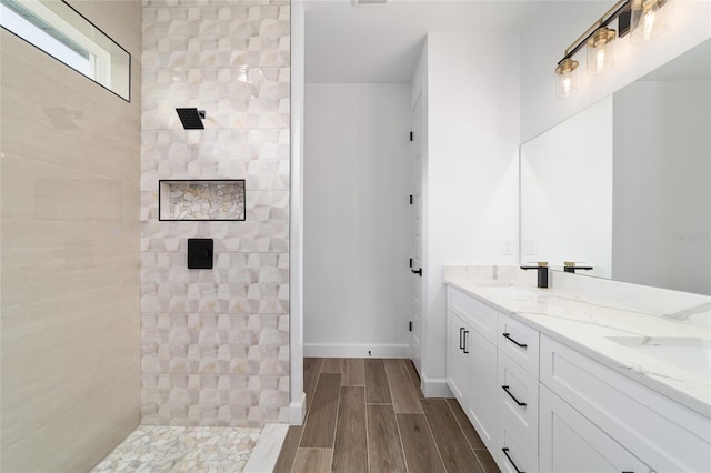full bath with a tile shower, wood finished floors, double vanity, and baseboards
