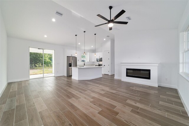 unfurnished living room featuring lofted ceiling, ceiling fan, wood finished floors, a glass covered fireplace, and baseboards