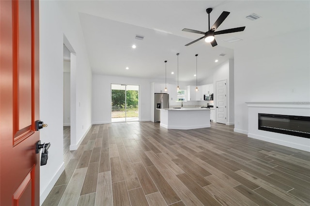 unfurnished living room featuring wood finished floors, a glass covered fireplace, ceiling fan, baseboards, and recessed lighting