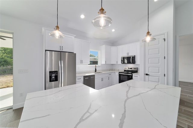 kitchen featuring appliances with stainless steel finishes, a sink, wood finished floors, white cabinets, and lofted ceiling