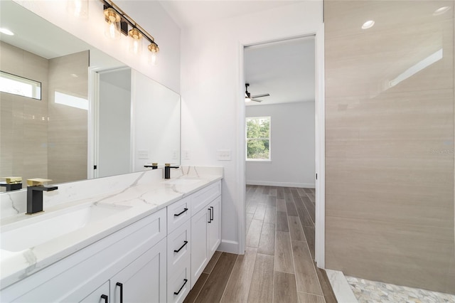 full bathroom featuring wood finished floors, ceiling fan, double vanity, and baseboards