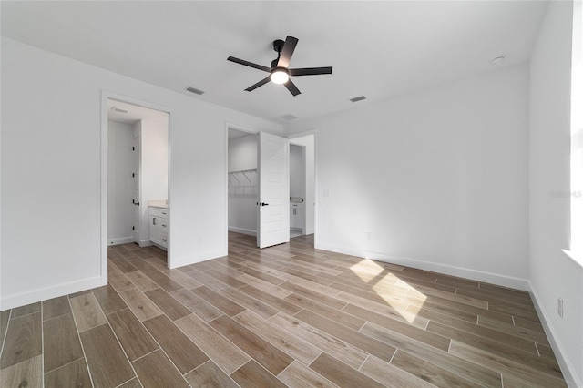 unfurnished bedroom featuring wood finished floors, baseboards, ceiling fan, and a walk in closet