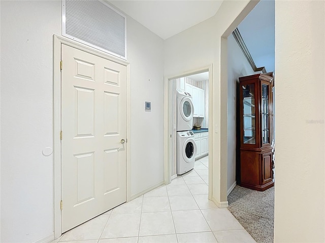 clothes washing area featuring stacked washing maching and dryer, light tile patterned floors, visible vents, and baseboards