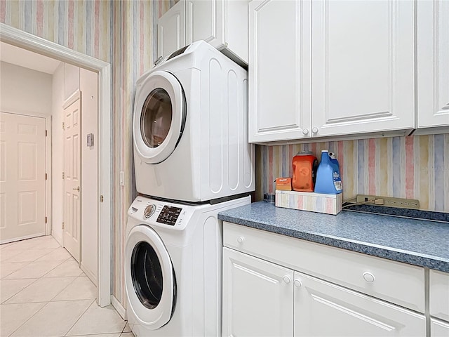 clothes washing area featuring cabinet space, light tile patterned floors, stacked washer and clothes dryer, and wallpapered walls