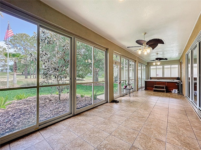 unfurnished sunroom with a textured ceiling, ceiling fan, a hot tub, and tile patterned floors