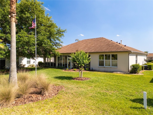 rear view of property featuring roof with shingles, a lawn, and stucco siding