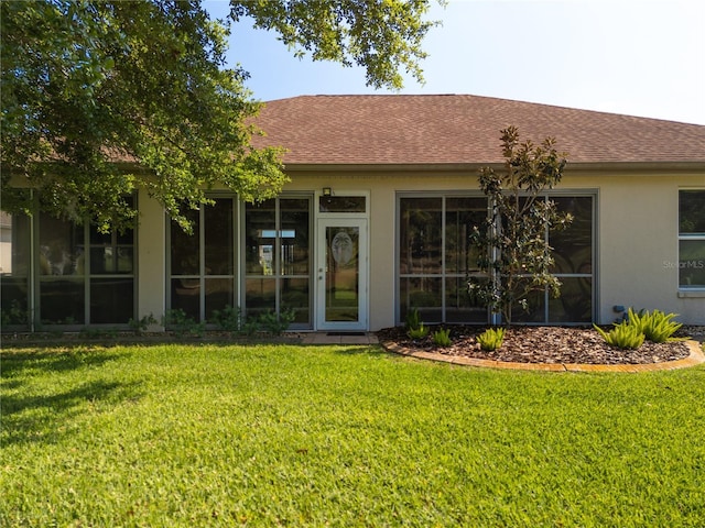 view of exterior entry with a yard, roof with shingles, and stucco siding