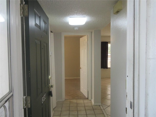 hall with light tile patterned flooring, a textured ceiling, and light carpet