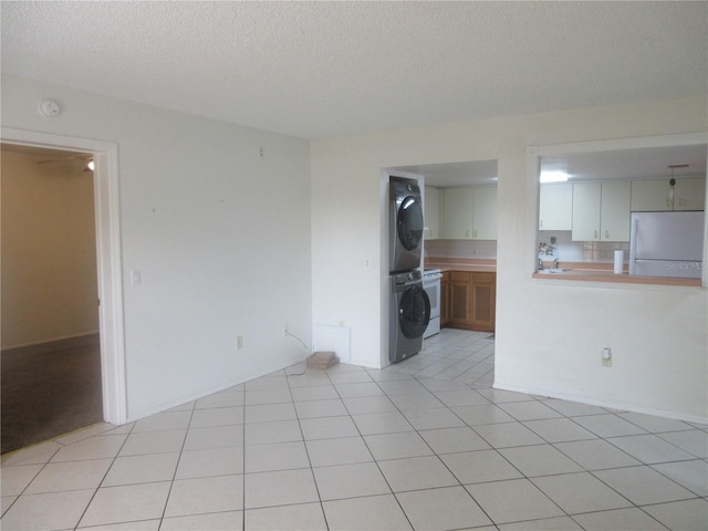 empty room with stacked washer and clothes dryer, a textured ceiling, and light tile patterned floors