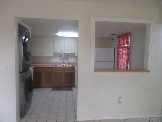 kitchen with light countertops, light tile patterned floors, a sink, freestanding refrigerator, and stacked washer and dryer