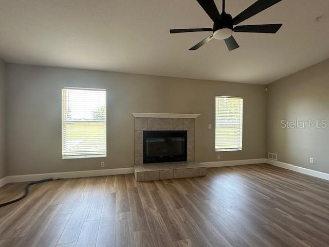 9934 SE 64th Ave, Belleview, FL 34420 - unfurnished living room featuring ceiling fan, visible vents, wood finished floors, a tiled fireplace, and baseboards