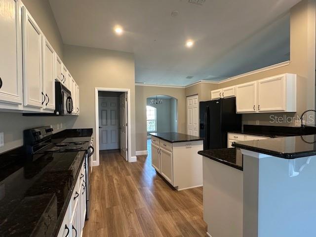 9934 SE 64th Ave, Belleview, FL 34420 - kitchen featuring dark countertops, a kitchen island, arched walkways, black appliances, and wood finished floors
