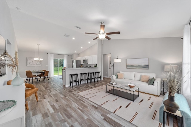 living room featuring visible vents, light wood-style flooring, high vaulted ceiling, and ceiling fan with notable chandelier