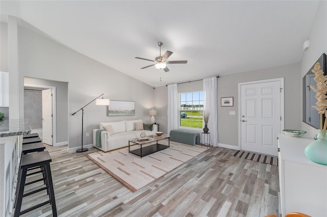 living area with baseboards, light wood-type flooring, a ceiling fan, and lofted ceiling