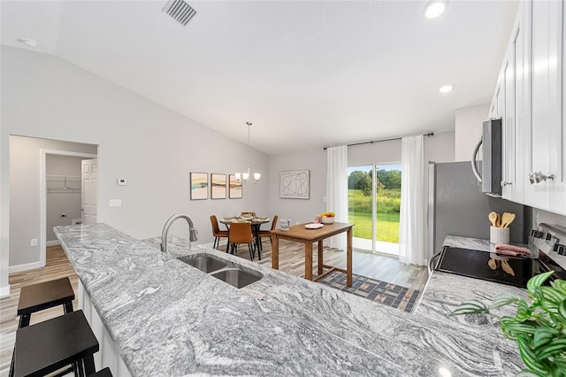 kitchen featuring stainless steel microwave, a breakfast bar, white cabinetry, lofted ceiling, and a sink