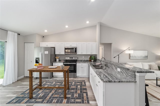 kitchen with dark stone countertops, white cabinets, a sink, appliances with stainless steel finishes, and a peninsula