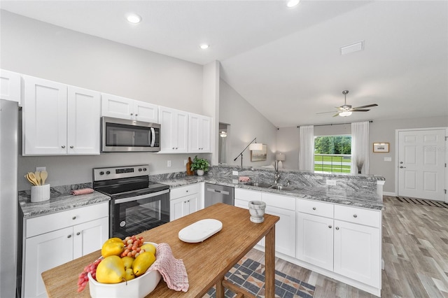 kitchen featuring a peninsula, white cabinets, a sink, lofted ceiling, and stainless steel appliances