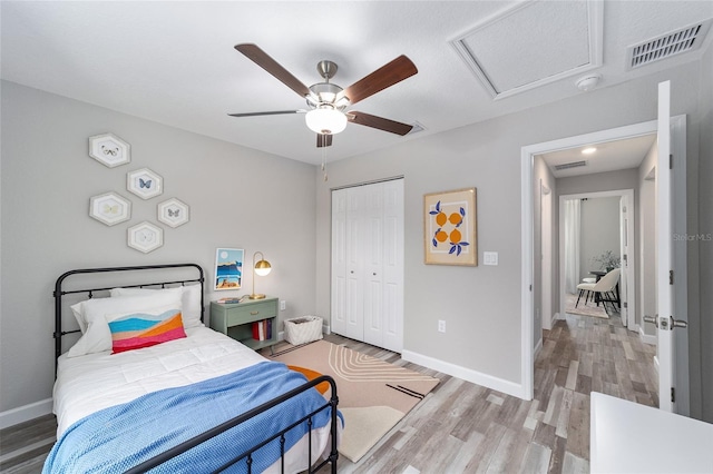 bedroom featuring visible vents, baseboards, a closet, light wood-style floors, and attic access