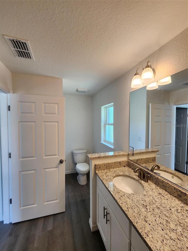 bathroom featuring vanity, toilet, a textured ceiling, wood finished floors, and visible vents