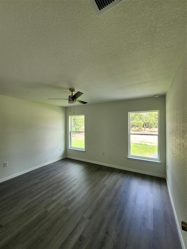 empty room with baseboards, dark wood finished floors, a textured wall, and visible vents