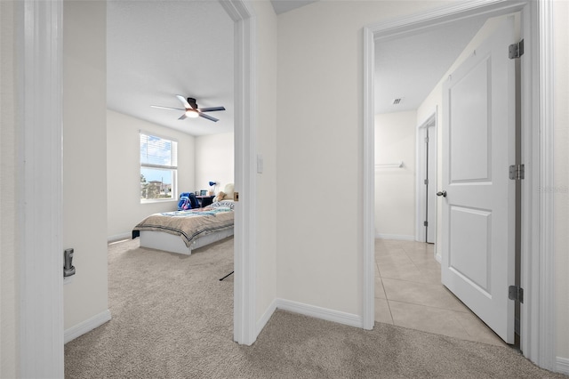 corridor featuring light tile patterned floors, baseboards, and light carpet