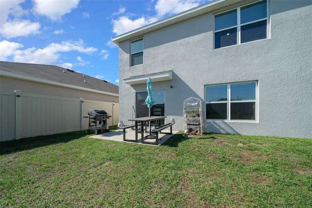 rear view of property featuring a patio, stucco siding, fence, and a lawn