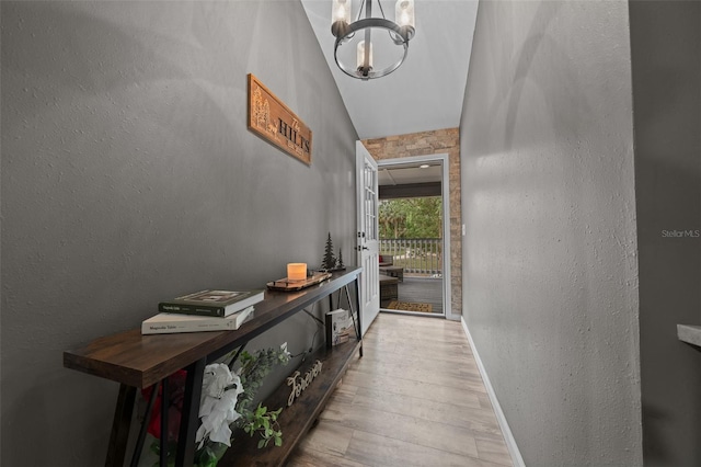 corridor with a textured wall, a notable chandelier, baseboards, and wood finished floors