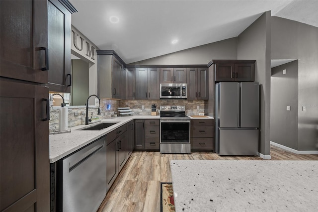 kitchen featuring appliances with stainless steel finishes, a sink, lofted ceiling, light wood finished floors, and decorative backsplash