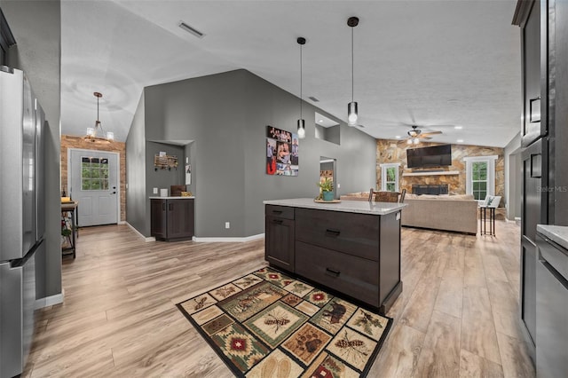 kitchen featuring a stone fireplace, freestanding refrigerator, a ceiling fan, light wood-style flooring, and lofted ceiling