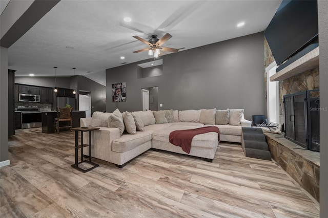 living room featuring light wood-style floors, a ceiling fan, a stone fireplace, and recessed lighting