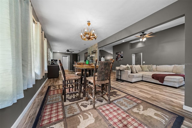 dining area with ceiling fan with notable chandelier, wood finished floors, and baseboards
