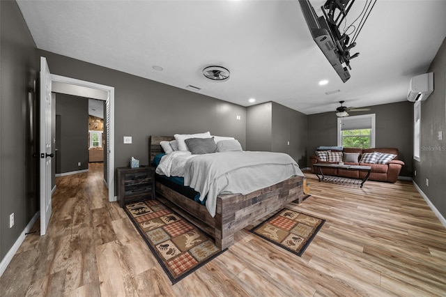 bedroom with light wood-style flooring, a wall unit AC, baseboards, and visible vents