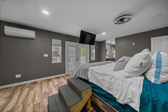 bedroom with baseboards, light wood-style floors, french doors, access to outside, and a wall unit AC