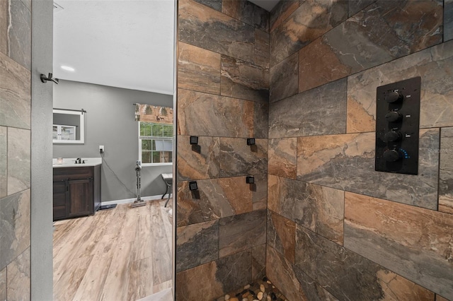 full bathroom with baseboards, tiled shower, vanity, and wood finished floors