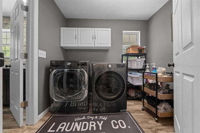 clothes washing area featuring light wood-style flooring, washing machine and clothes dryer, cabinet space, and a wealth of natural light