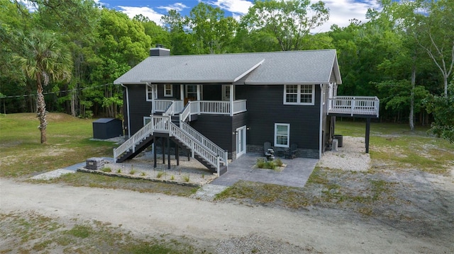 view of front of property with roof with shingles, a chimney, stairway, a front lawn, and a patio area