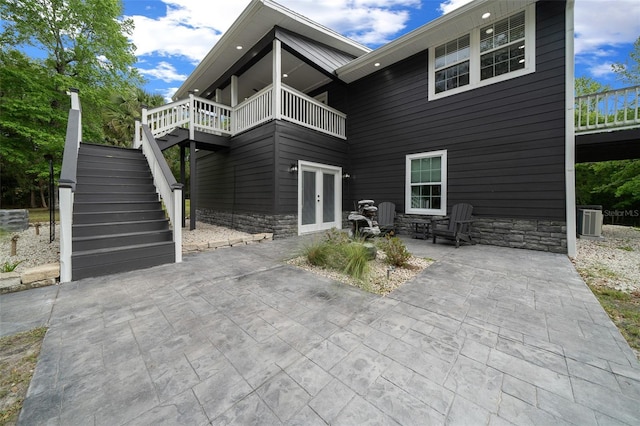 rear view of property featuring a patio, stairway, french doors, stone siding, and central AC