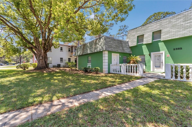front of property featuring roof with shingles, stucco siding, mansard roof, and a front lawn
