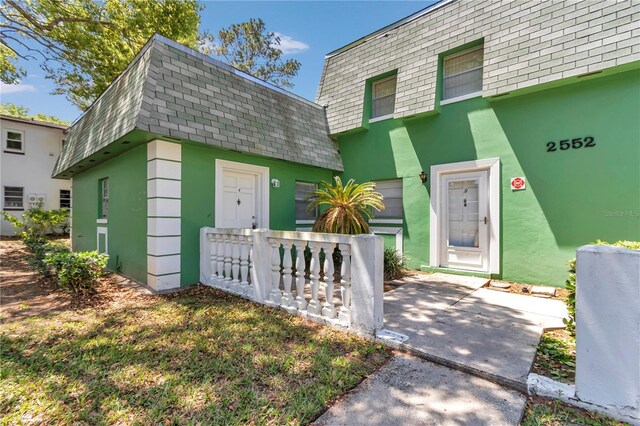 entrance to property with mansard roof, a shingled roof, and stucco siding
